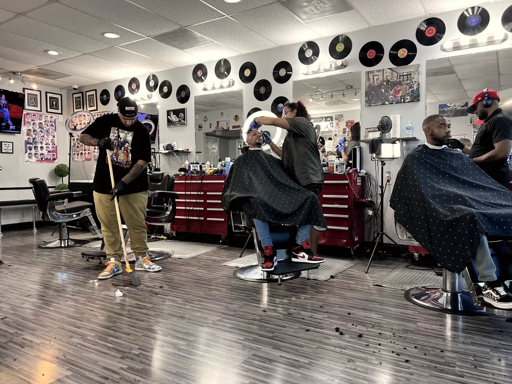 The shop floor under a wall of vinyl records, barbers at work